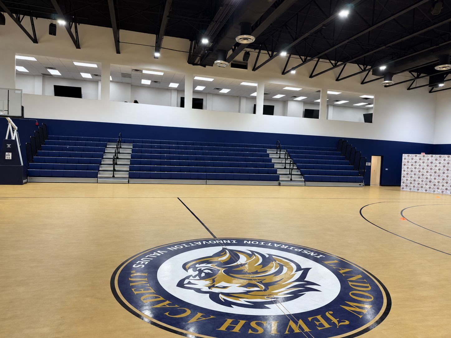 Landow’s indoor gymnasium with basketball court, Lions center-court logo, and spectator bleachers